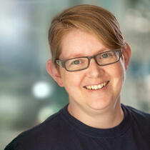 A photo of a person wearing glasses who is in a space with large columns made of light coloured bricks